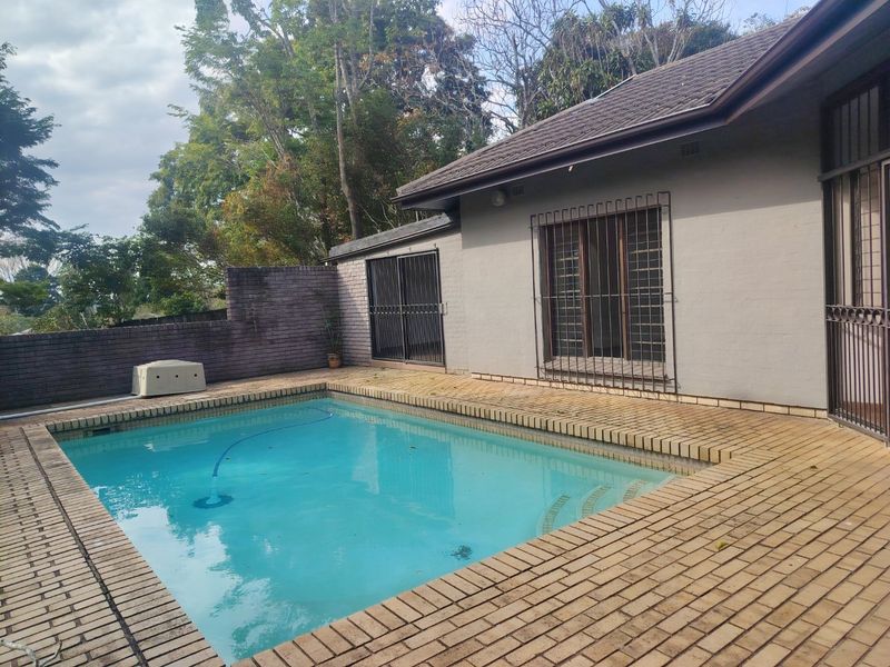 Rear exterior view featuring a swimming pool with brick paving surround, security bars on windows, and a brick boundary wall.