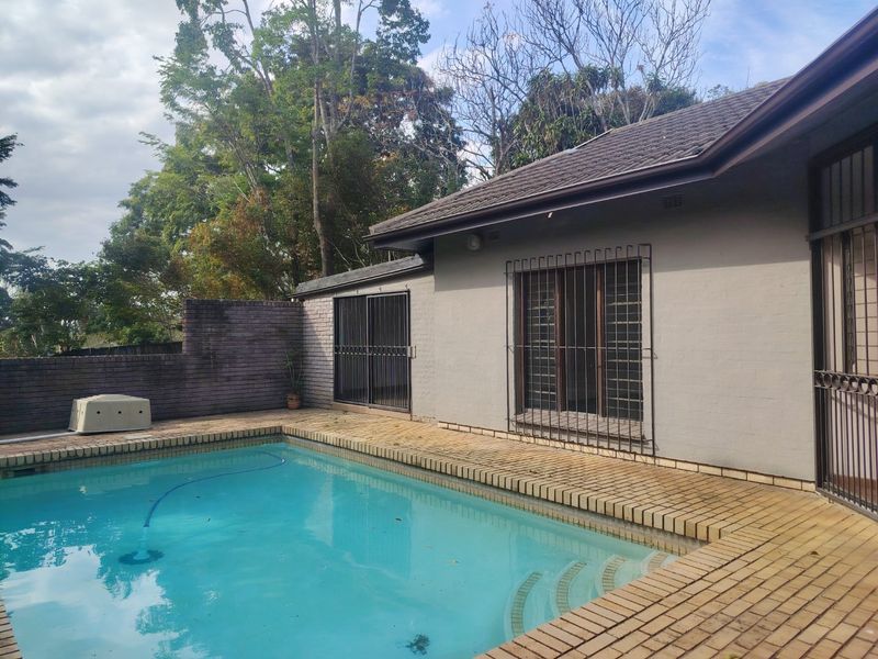 Outdoor pool area featuring a swimming pool with brick coping, security bars on windows, and a surrounding brick boundary wall.