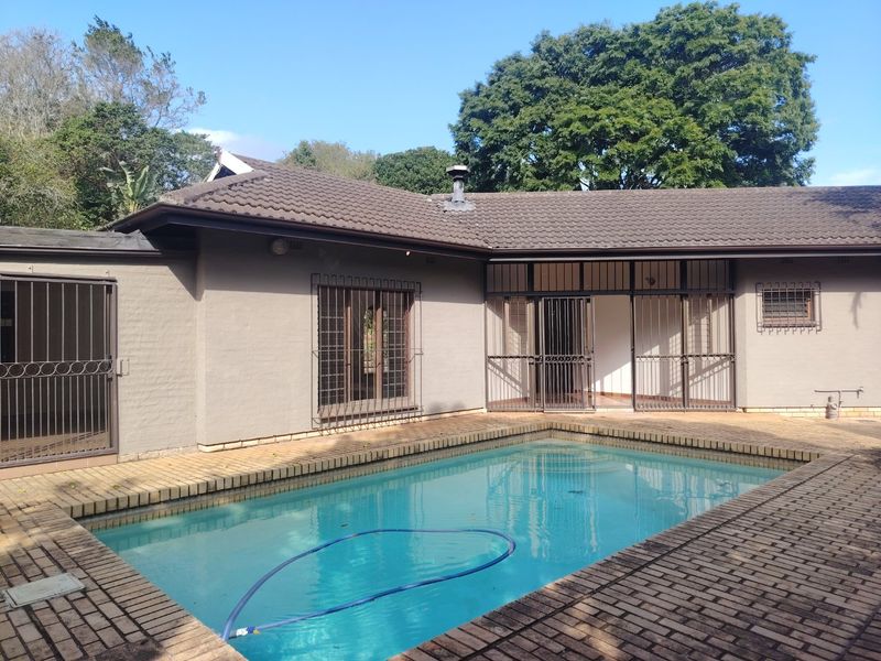A rear exterior view featuring a swimming pool with brick paving surround, security gates, and a tiled roof structure.