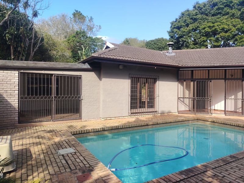 A rear exterior view featuring a swimming pool with brick paving, security gates on sliding doors, and a tiled roof structure.