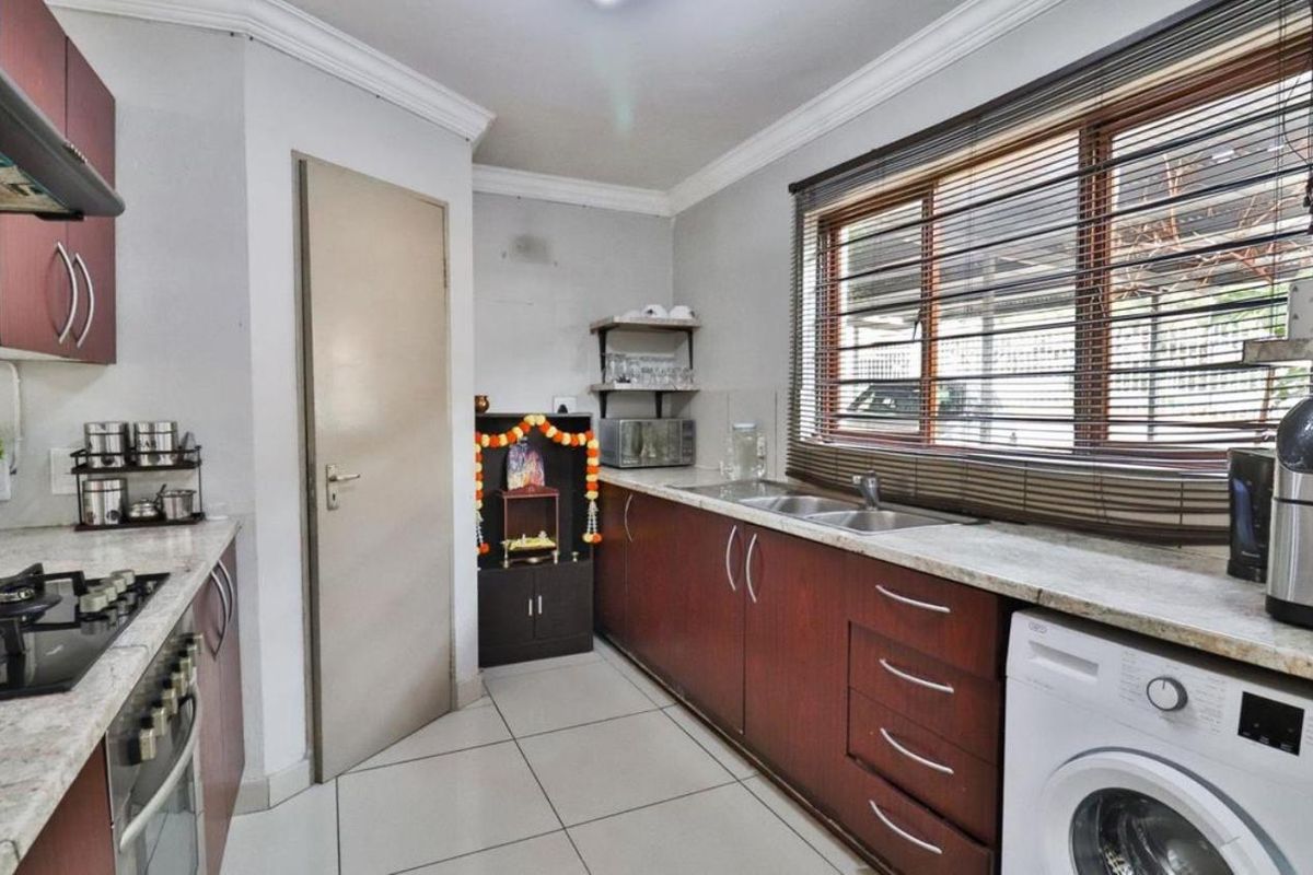 A functional kitchen featuring dark wood cabinetry, stone countertops, a gas hob, and integrated laundry plumbing, finished with tiled flooring and coving.