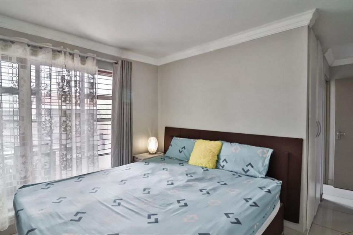 A well-maintained bedroom featuring neutral wall tones, tiled flooring, decorative cornice, and built-in cupboard storage.
