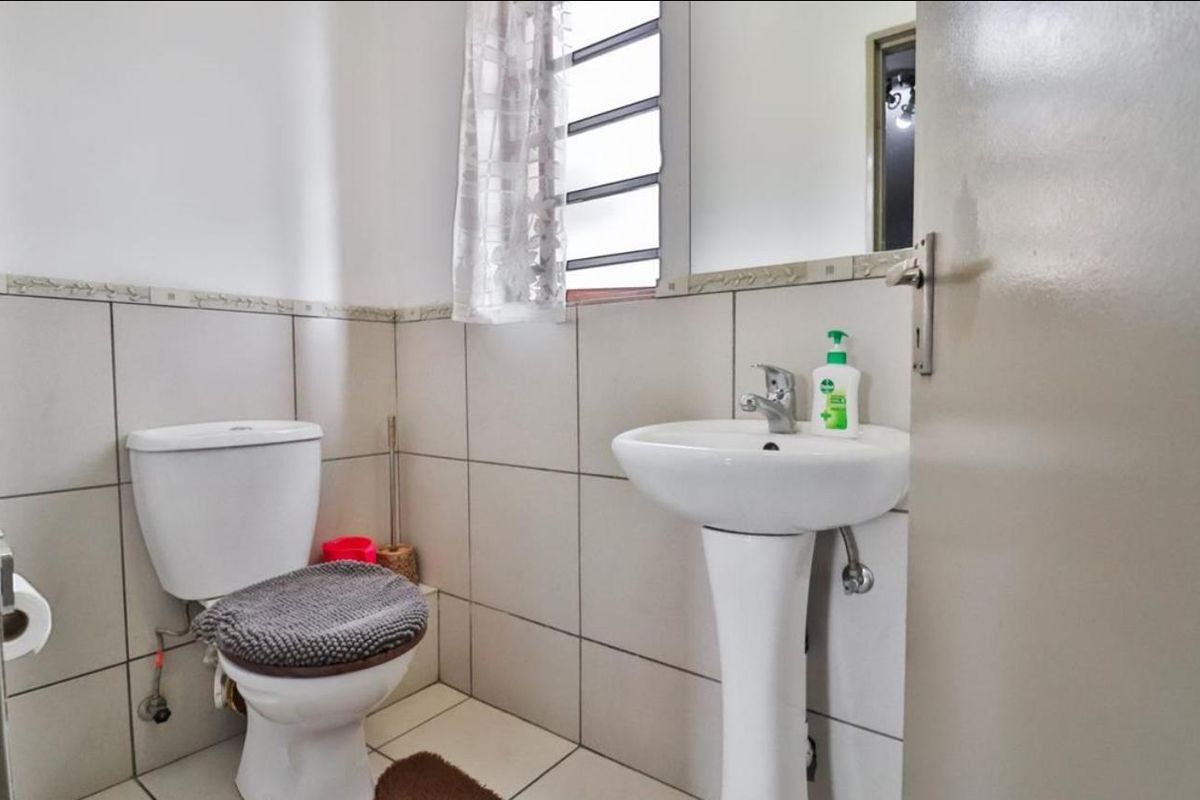 A functional bathroom featuring a pedestal basin, toilet, and neutral wall tiling with a louvered window for natural ventilation.
