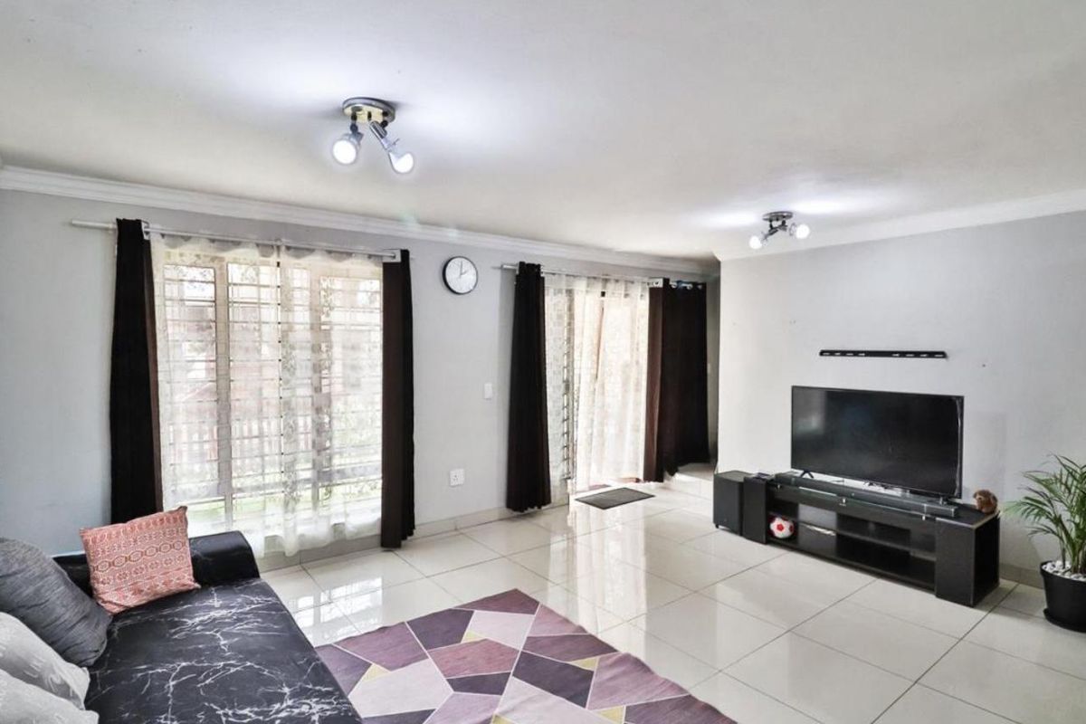 A bright living room featuring large tiled floors, ceiling spotlights, and sliding glass doors providing access to the exterior.