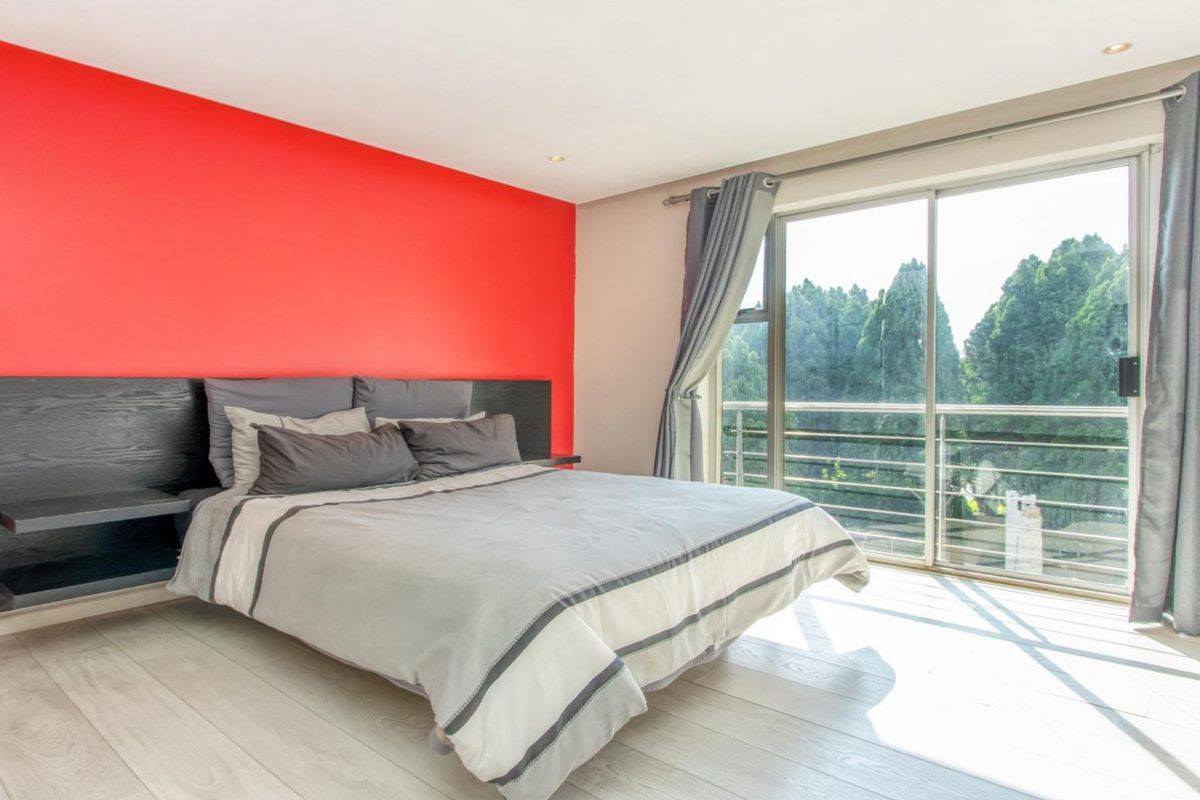 A bright bedroom featuring laminate flooring, a bold red accent wall, and large sliding glass doors that open to a balcony with scenic views.