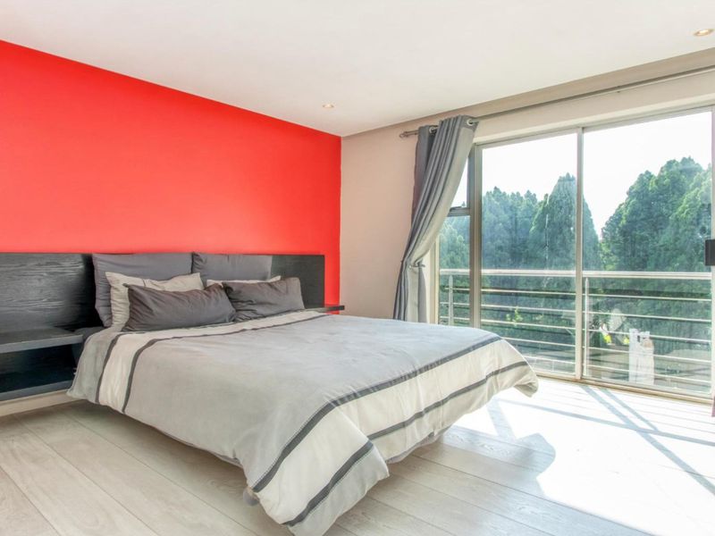 A bright bedroom featuring laminate flooring, a bold red accent wall, and large sliding glass doors that open to a balcony with scenic views.