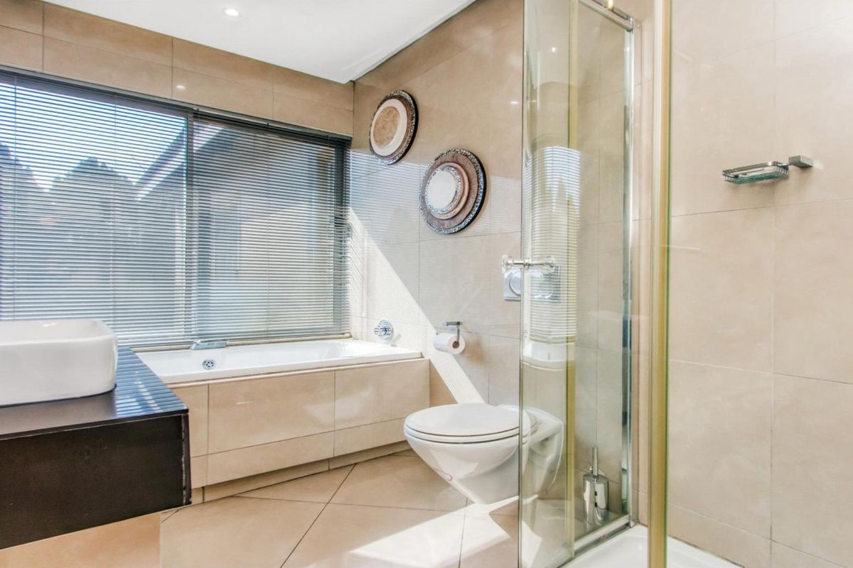 Modern bathroom featuring a built-in bathtub, wall-mounted toilet, glass shower enclosure, and neutral tiled finishes throughout.