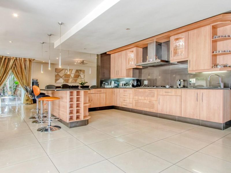 Spacious open-plan kitchen featuring light wood cabinetry, a breakfast bar, and modern tiled flooring, seamlessly flowing into the living area.