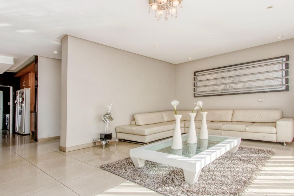A bright and spacious living room featuring neutral tiled flooring, recessed downlighting, and a modern crystal chandelier, creating a clean and inviting atmosphere.