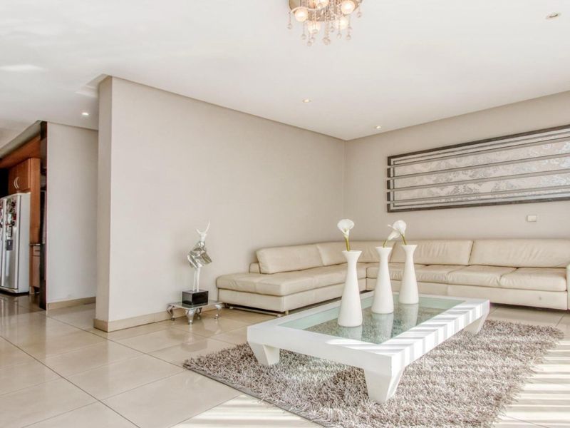 A bright and spacious living room featuring neutral tiled flooring, recessed downlighting, and a modern crystal chandelier, creating a clean and inviting atmosphere.