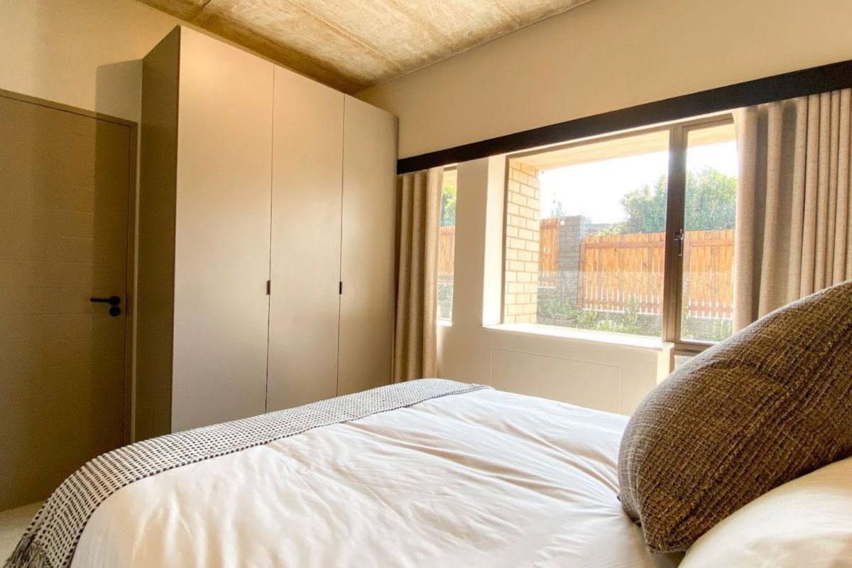 A well-maintained bedroom featuring built-in cupboards, an exposed concrete ceiling, and a large window providing natural light.