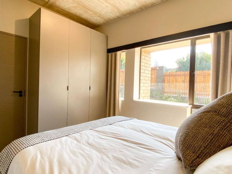 A well-maintained bedroom featuring built-in cupboards, an exposed concrete ceiling, and a large window providing natural light.