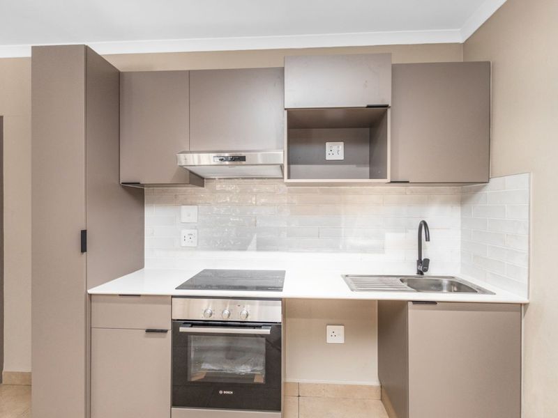 Modern compact kitchen featuring sleek taupe cabinetry, quartz countertops, subway tile backsplash, and integrated Bosch oven and hob.