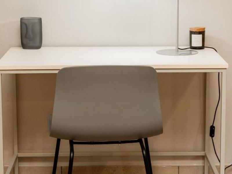 A functional workspace area featuring a desk and wall-mounted electrical outlet, suitable for a home office setup.