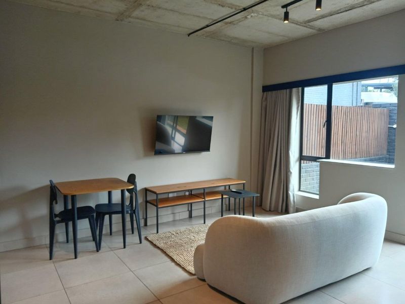 Modern open-plan living area featuring an exposed concrete ceiling, track lighting, and large windows that provide ample natural light.