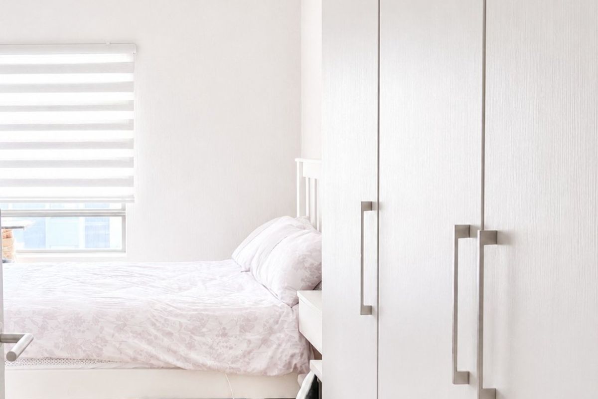 A bright bedroom featuring light-toned laminate flooring, a built-in wardrobe with modern handles, and a window fitted with a roller blind.