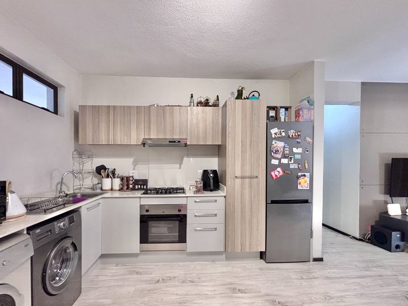 Modern open-plan kitchen featuring light wood-grain cabinetry, gas hob, built-in oven, and integrated laundry appliances, seamlessly flowing into the adjacent living area.