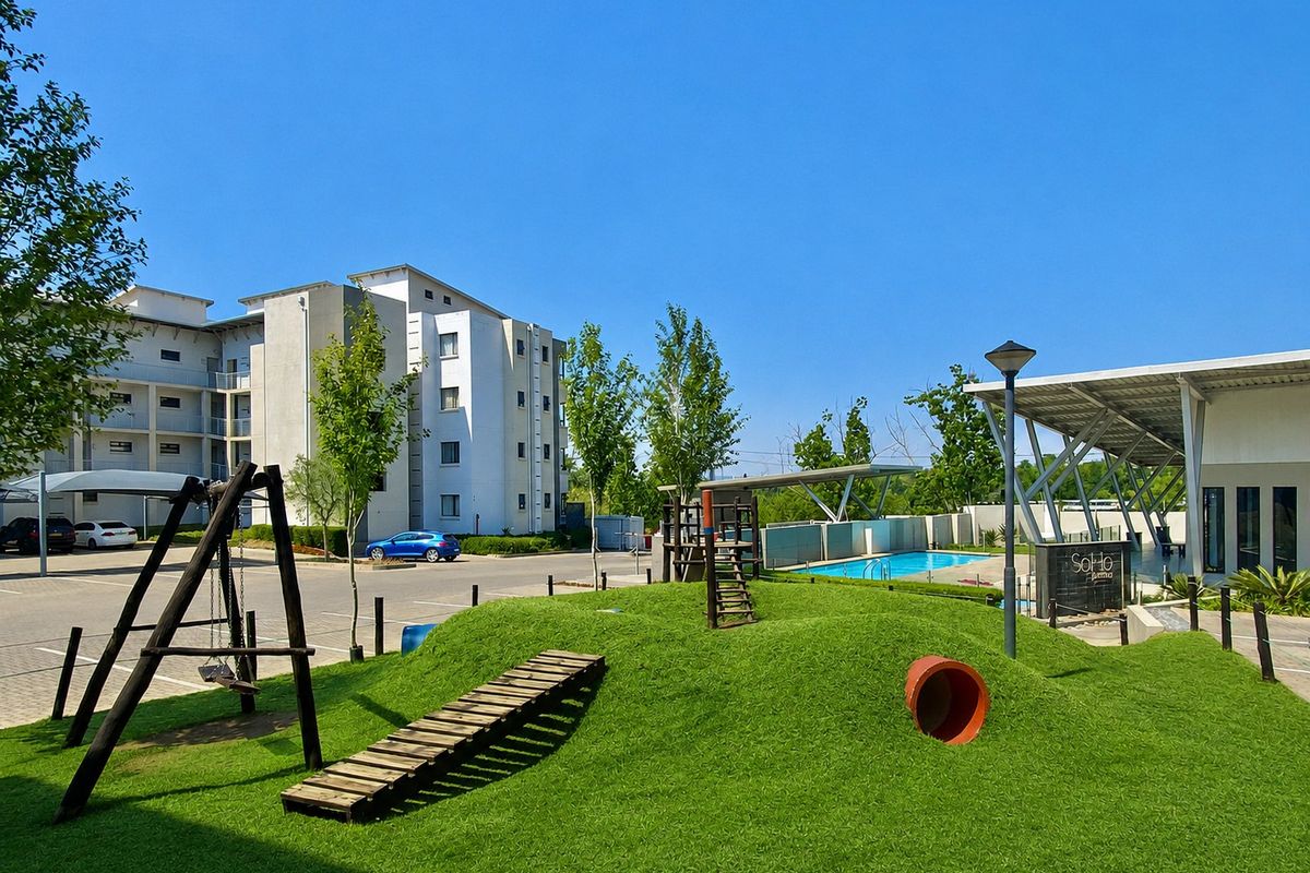 Communal outdoor area featuring a swimming pool, playground equipment, and landscaped artificial turf within an apartment complex.