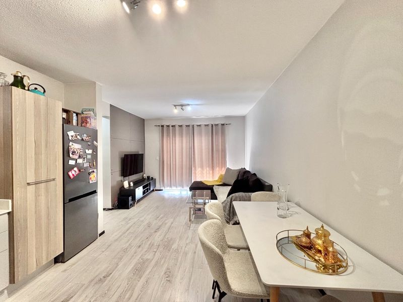An open-plan living and dining area featuring light wood-look laminate flooring, modern ceiling lighting, and a feature wall panel behind the television area.