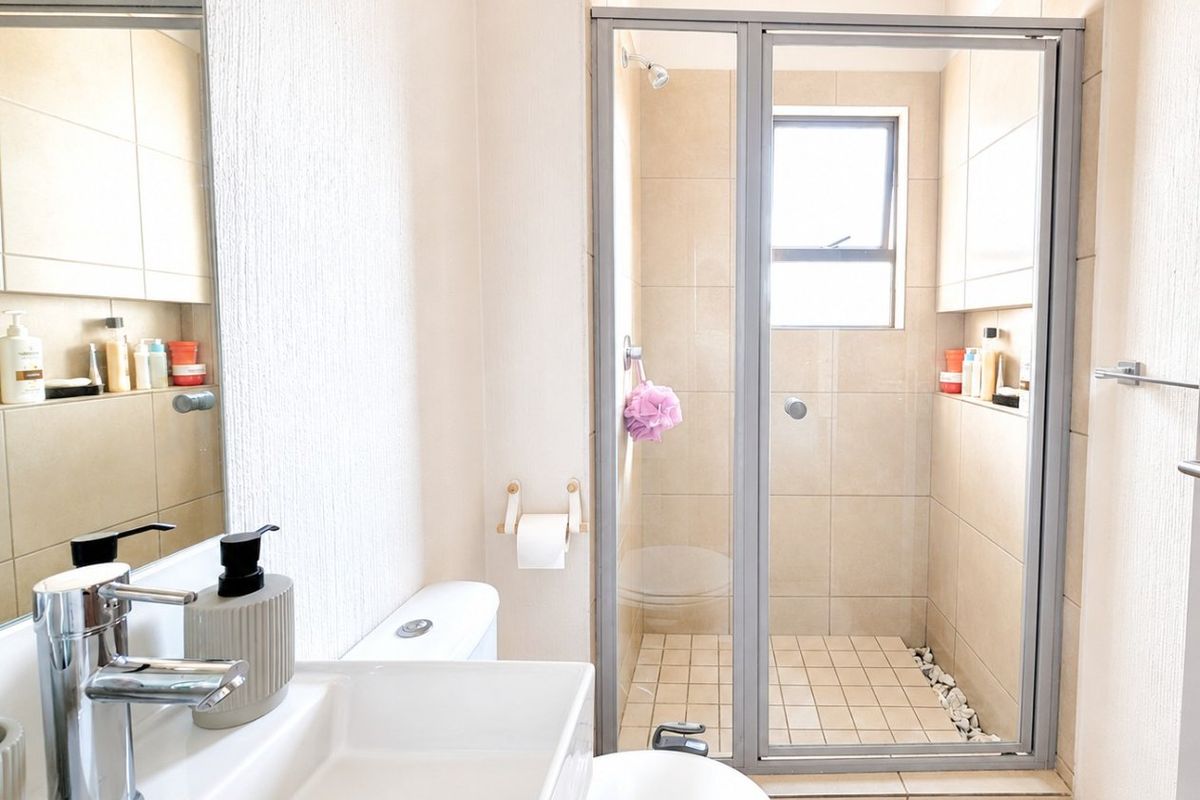 A clean and well-maintained bathroom featuring a tiled shower enclosure, modern vanity basin with chrome mixer tap, and neutral wall tiling.