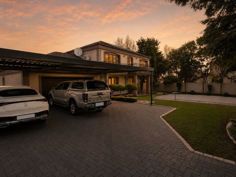 Front exterior view of a two-story house featuring a paved driveway, covered carport, and well-maintained landscaped garden at sunset.