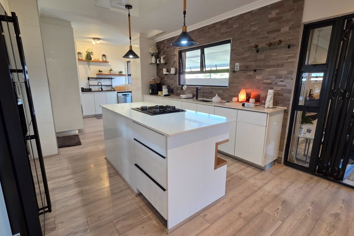 Modern kitchen featuring a central island with gas cooktop, stone countertops, sleek white cabinetry, and a stylish brick veneer feature wall.