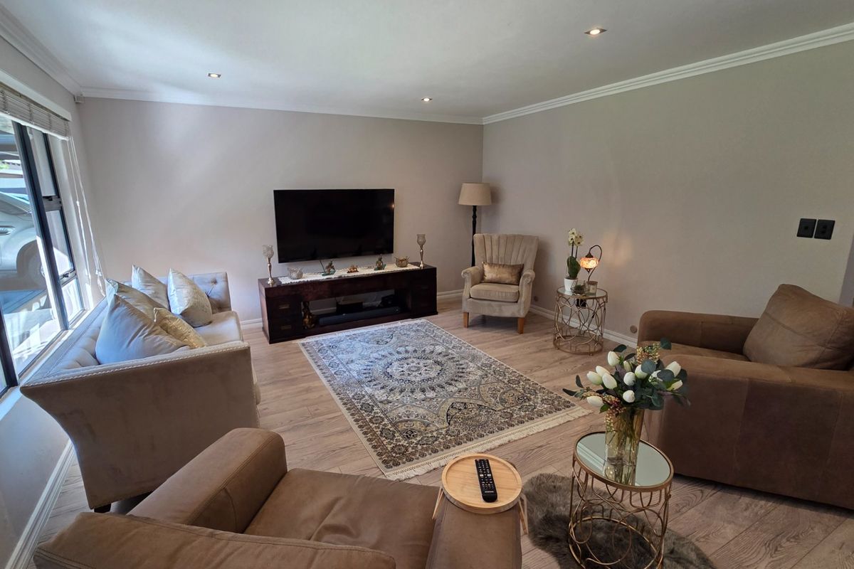 A well-maintained living room featuring light-toned laminate flooring, recessed downlighting, and coved cornicing, creating a bright and comfortable atmosphere.