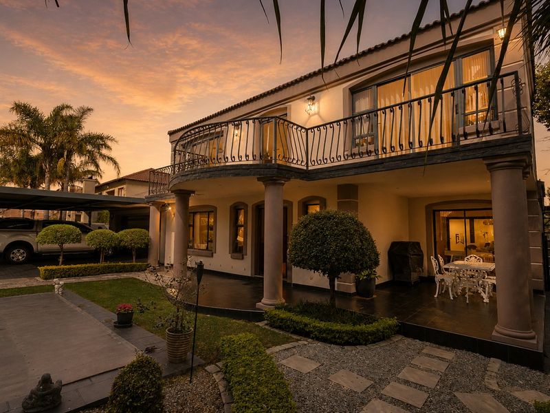 A well-maintained double-story rear elevation featuring a spacious covered patio, an upper-level balcony with wrought iron railings, and a landscaped garden area.