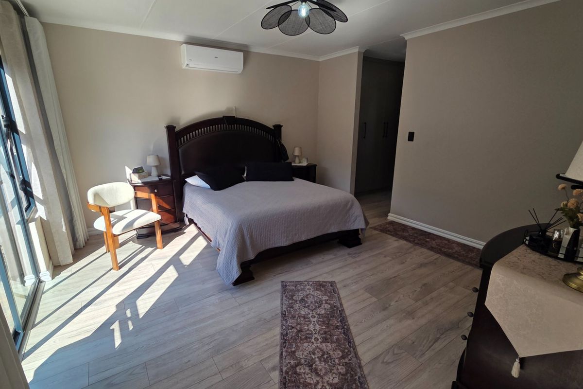 A well-maintained bedroom featuring light laminate flooring, built-in cupboards, and a wall-mounted air conditioning unit with access to an outdoor area via sliding doors.