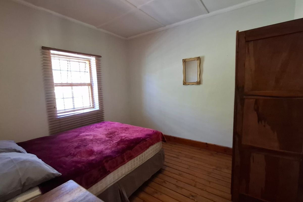 A bedroom featuring original timber flooring and a sash window with venetian blinds, offering a blank canvas for potential cosmetic updates.
