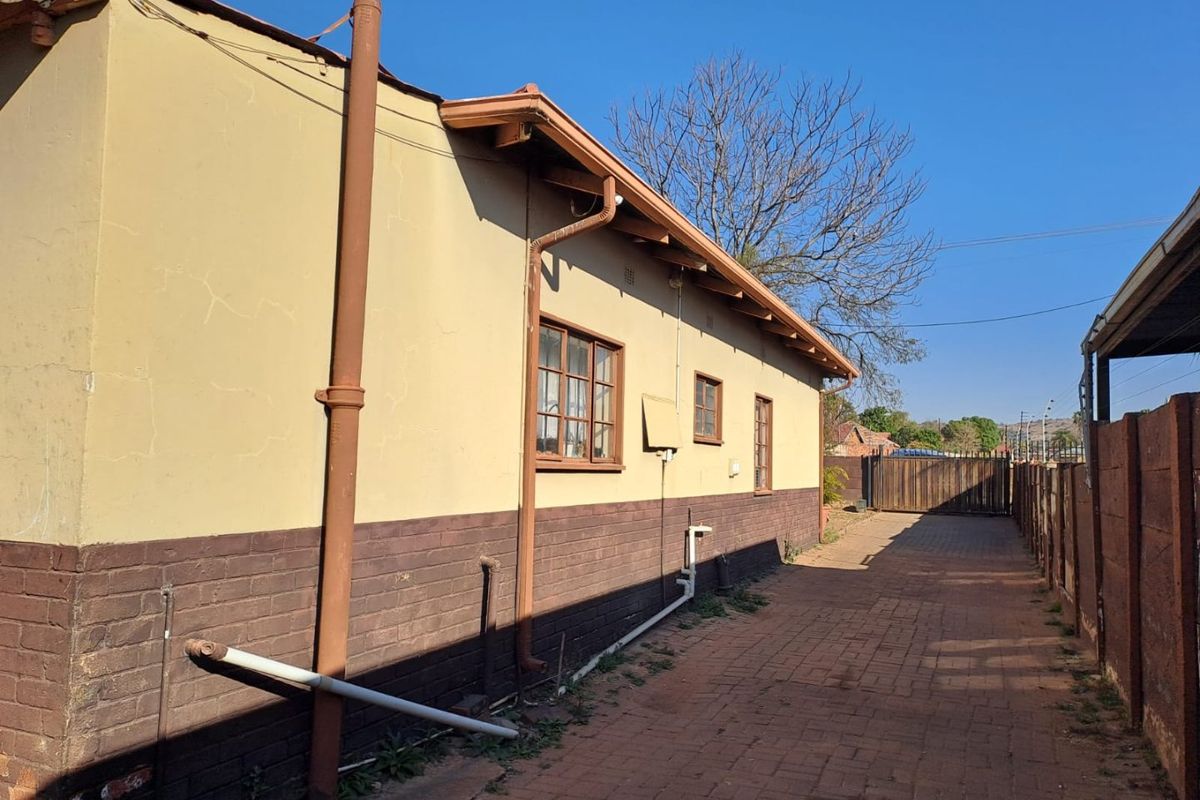 Side view of the property showing brick paving, exterior wall finishes, and drainage infrastructure along the side of the house.