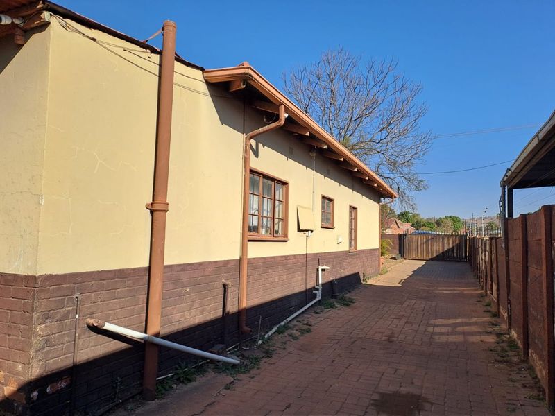 Side view of the property showing brick paving, exterior wall finishes, and drainage infrastructure along the side of the house.