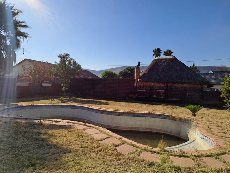 Backyard area featuring an empty swimming pool, paved surround, and a traditional thatched lapa structure set against a boundary wall.