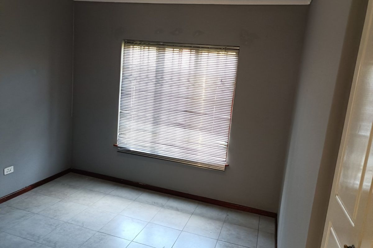 An empty bedroom featuring neutral grey walls, tiled flooring, and fitted venetian blinds, offering a blank canvas for personalization.