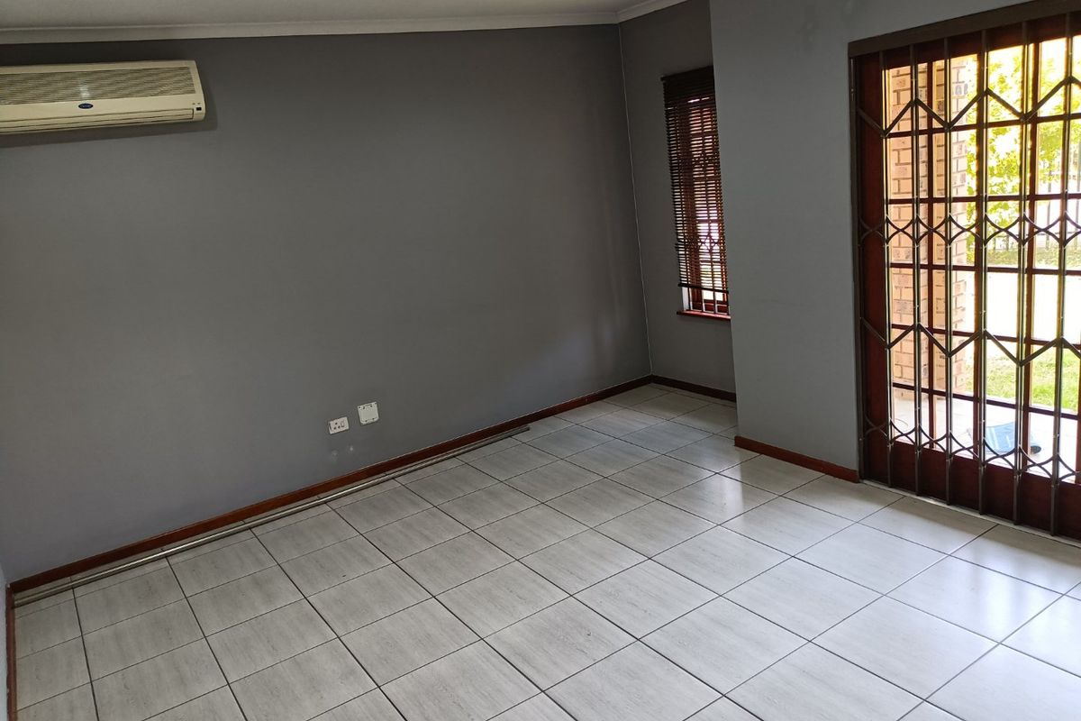 An empty living room featuring grey walls, tiled flooring, a split-system air conditioner, and a secure metal gate leading to the exterior.