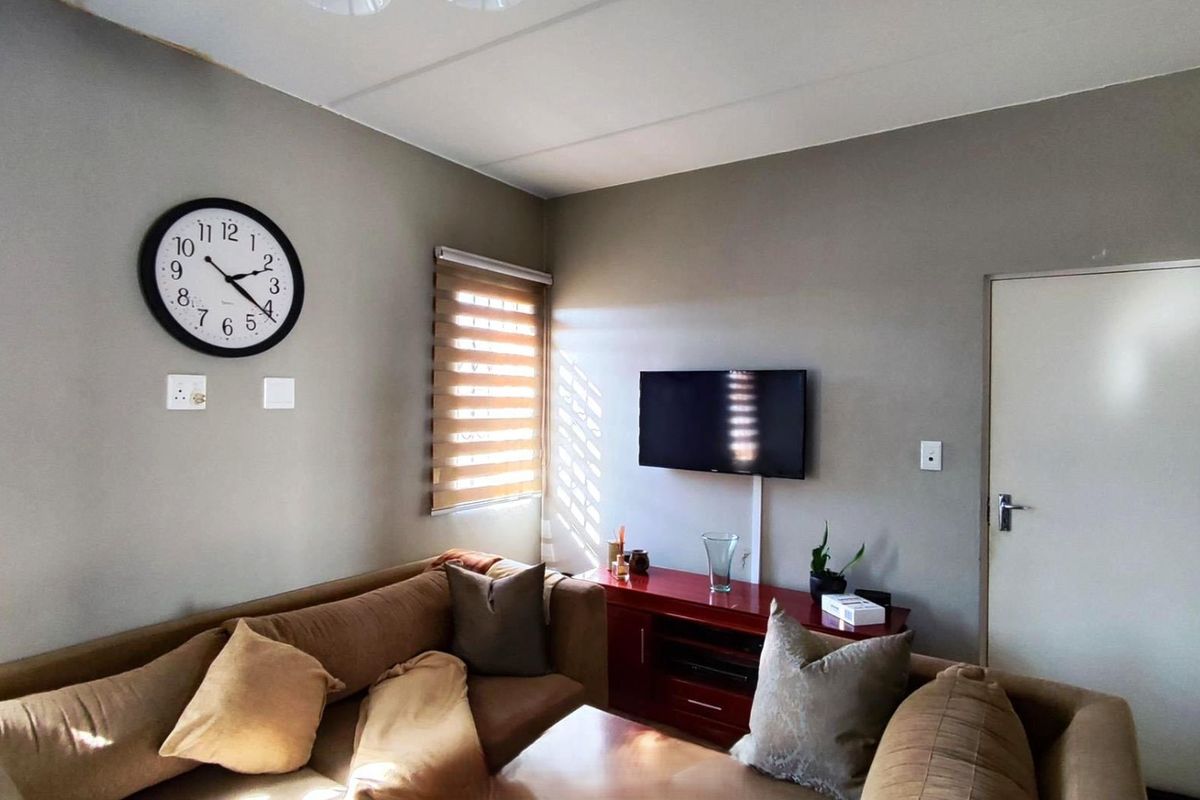 A living room featuring neutral wall tones, roller blinds, and a wall-mounted television setup.