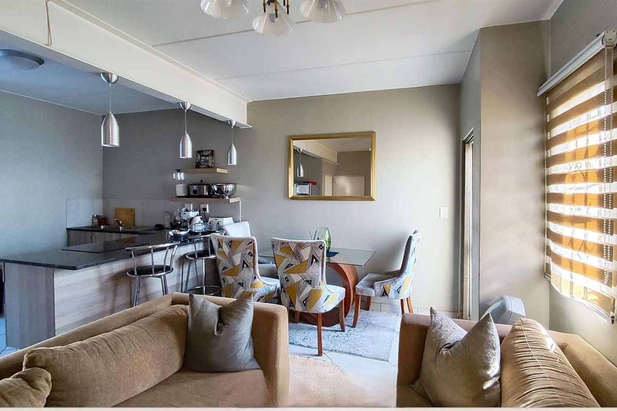 Open-plan living and dining area featuring a functional kitchen with breakfast bar, modern pendant lighting, and neutral finishes throughout.