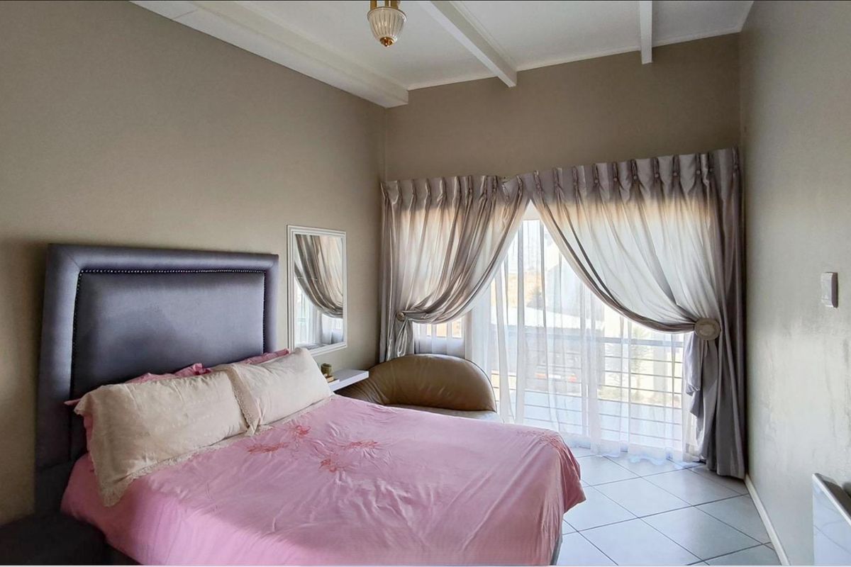 A bedroom featuring tiled flooring, exposed ceiling beams, and a large sliding glass door providing access to an outdoor area.
