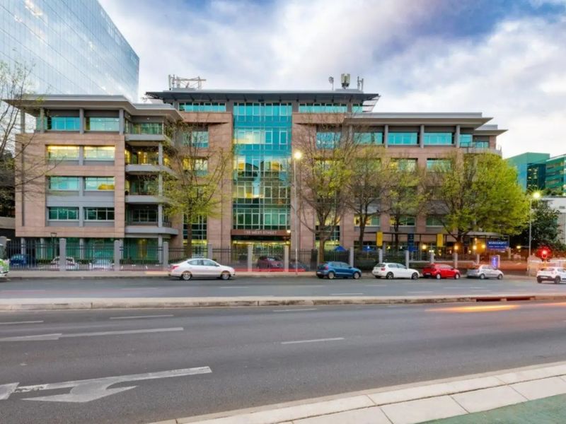 A professional street-level view of a multi-story commercial office building featuring a modern glass and stone facade with secure perimeter fencing.