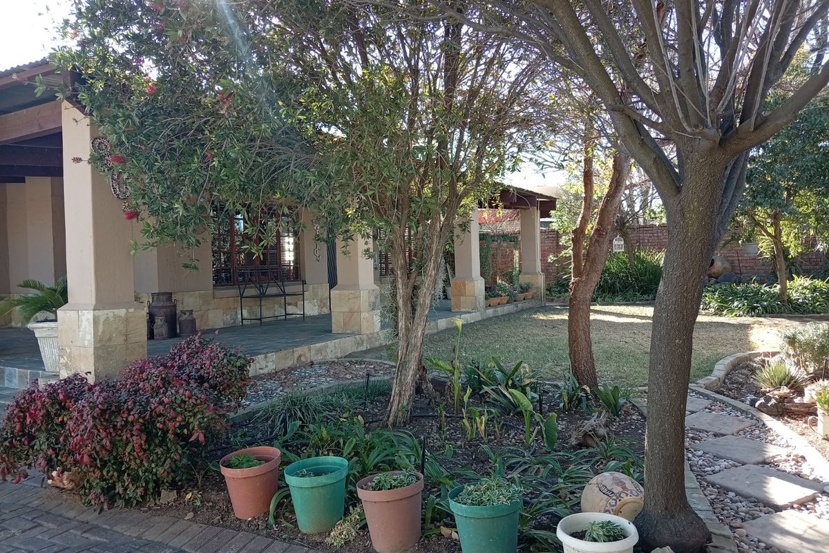 A view of the rear garden featuring a covered patio with stone-clad pillars, mature trees, and a paved walkway.