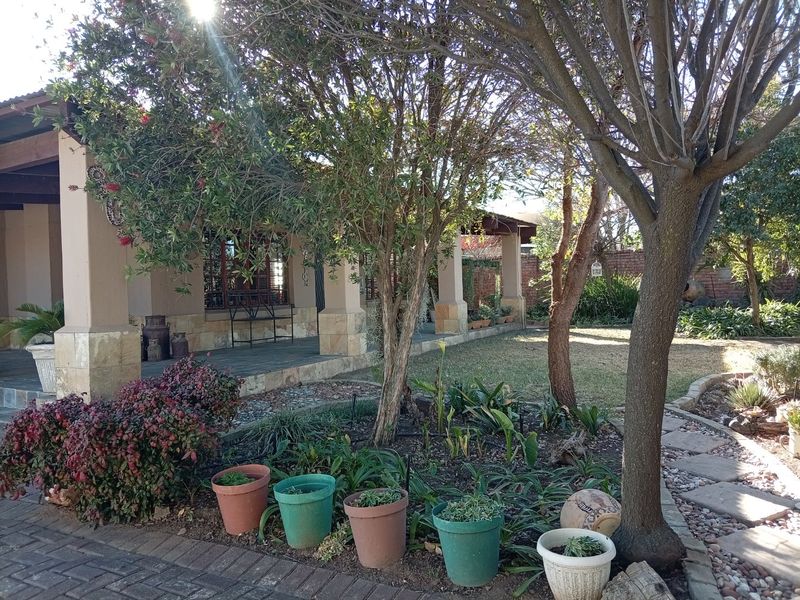 A view of the rear garden featuring a covered patio with stone-clad pillars, mature trees, and a paved walkway.