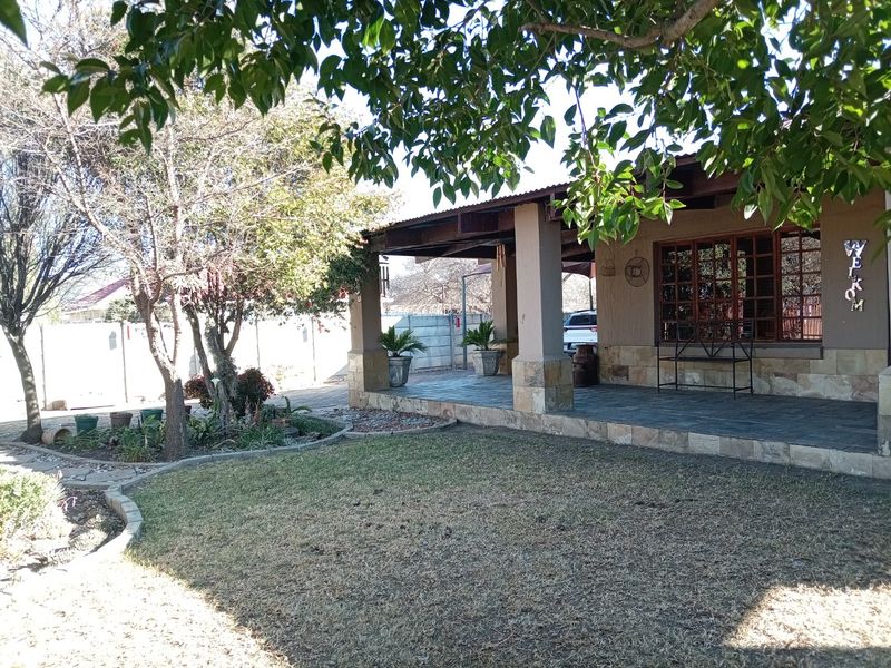 A covered patio area featuring stone-clad pillars and tiled flooring, overlooking a landscaped garden with mature trees and a brick boundary wall.