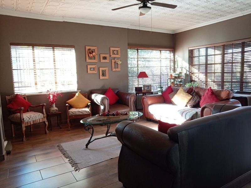 A spacious living room featuring tiled flooring, decorative ceiling tiles, a ceiling fan, and large windows fitted with venetian blinds.