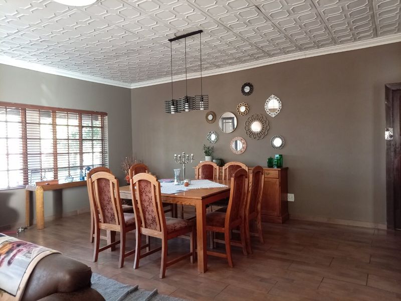 Spacious dining room featuring a decorative coffered ceiling, tiled flooring, and large windows with venetian blinds, creating a warm and inviting atmosphere.