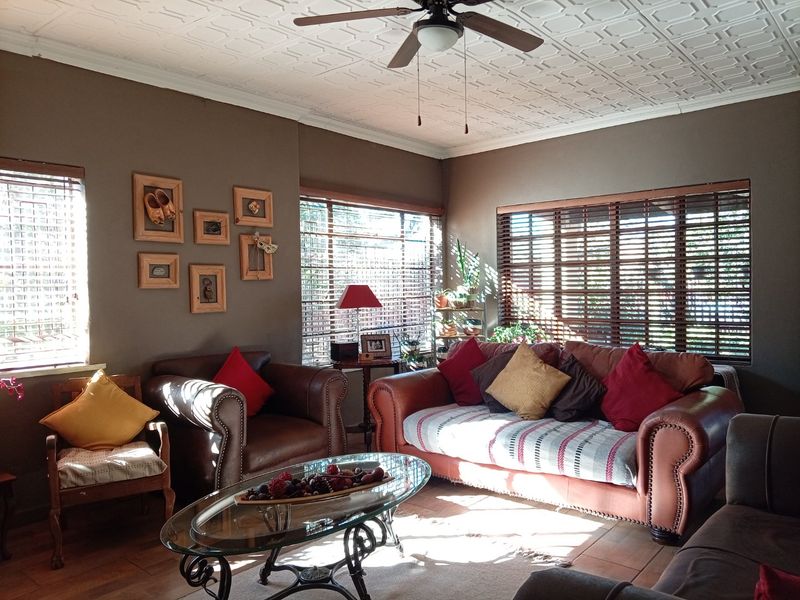 A comfortable living room featuring tiled flooring, a textured ceiling with a central fan, and large windows fitted with wooden blinds.