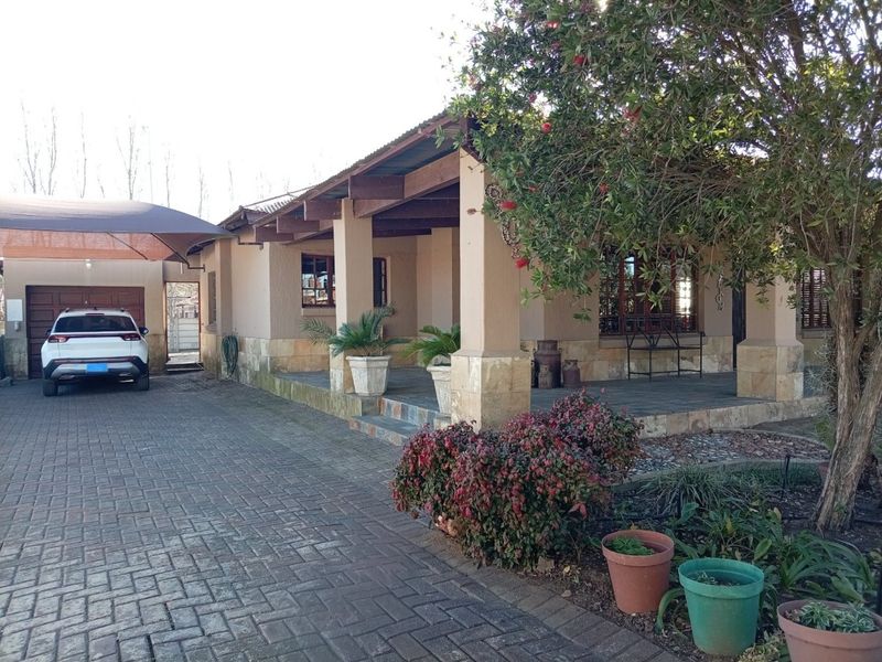 Front view of the house featuring a paved driveway, covered patio area with stone cladding, and an attached garage with a shade sail.