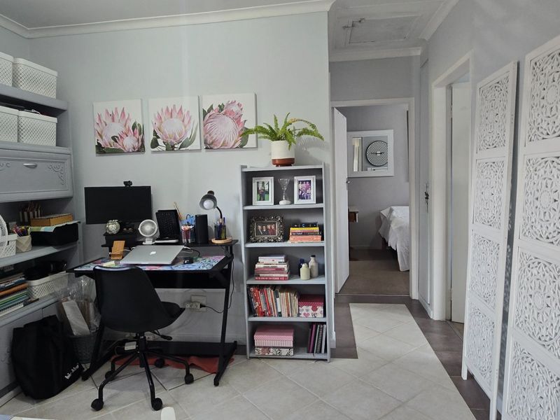 A functional home office space featuring tiled flooring and neutral wall finishes, with direct access to the hallway and adjacent bedroom.