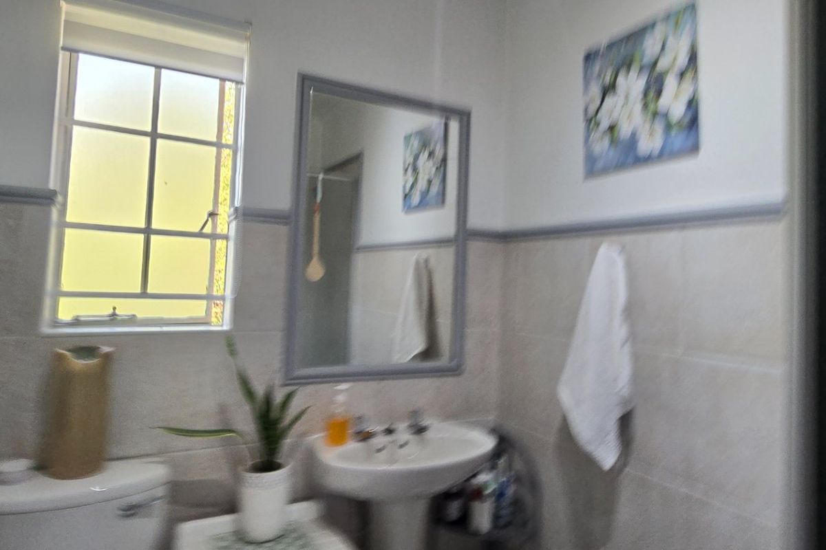 A functional bathroom featuring a pedestal basin, toilet, and neutral wall tiling with a window providing natural light.