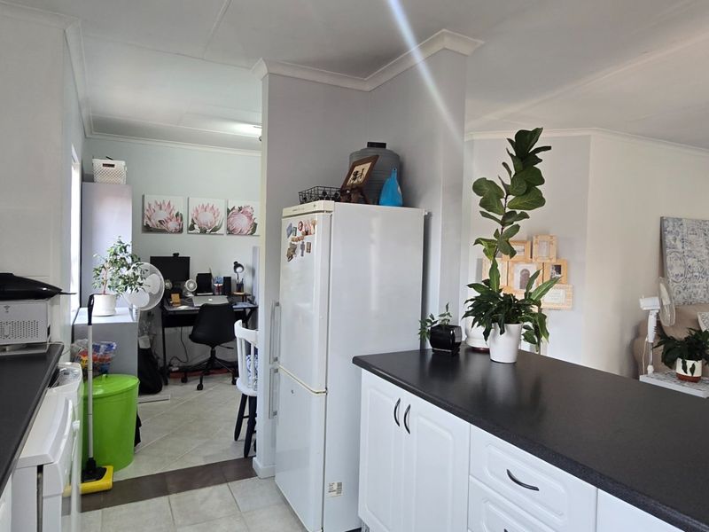 Open-plan kitchen area featuring white cabinetry, dark countertops, and tiled flooring, seamlessly connecting to the adjacent living and workspace areas.