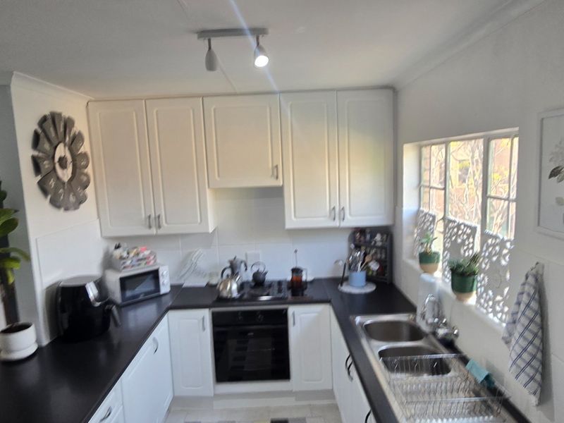 A functional kitchen featuring white cabinetry, black countertops, a built-in oven, and a stainless steel double sink with natural light from the side window.